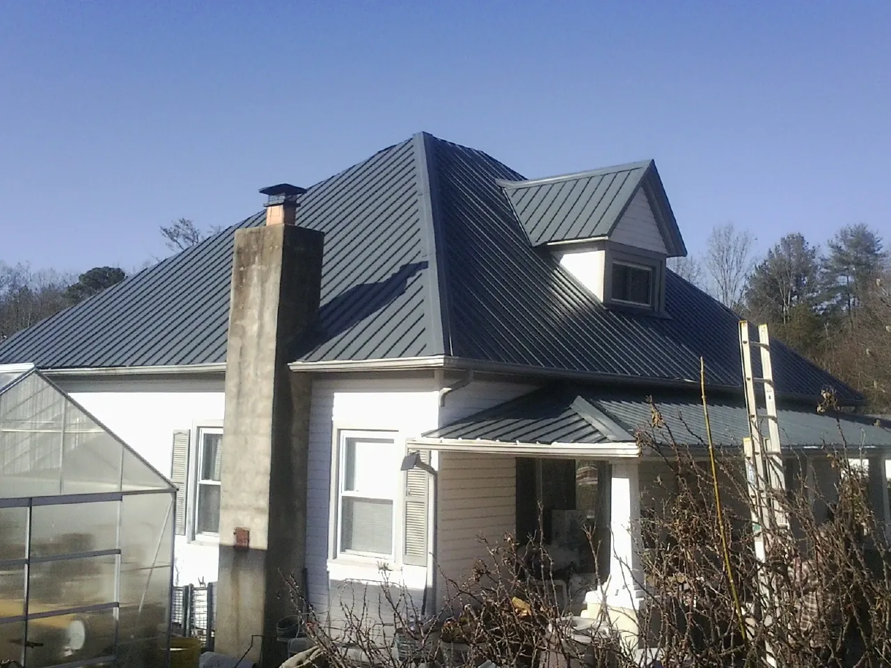 Dark blue standing seam metal roof on a white farmhouse with dormer — Slate & Tile Roof Repair by Roofing Brothers in Marmora