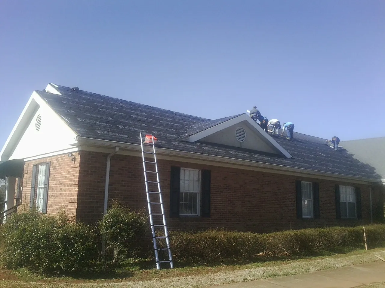 Crew tearing shingles off a brick ranch roof with a ladder set — Emergency Roof Repair work by our crew in Marmora