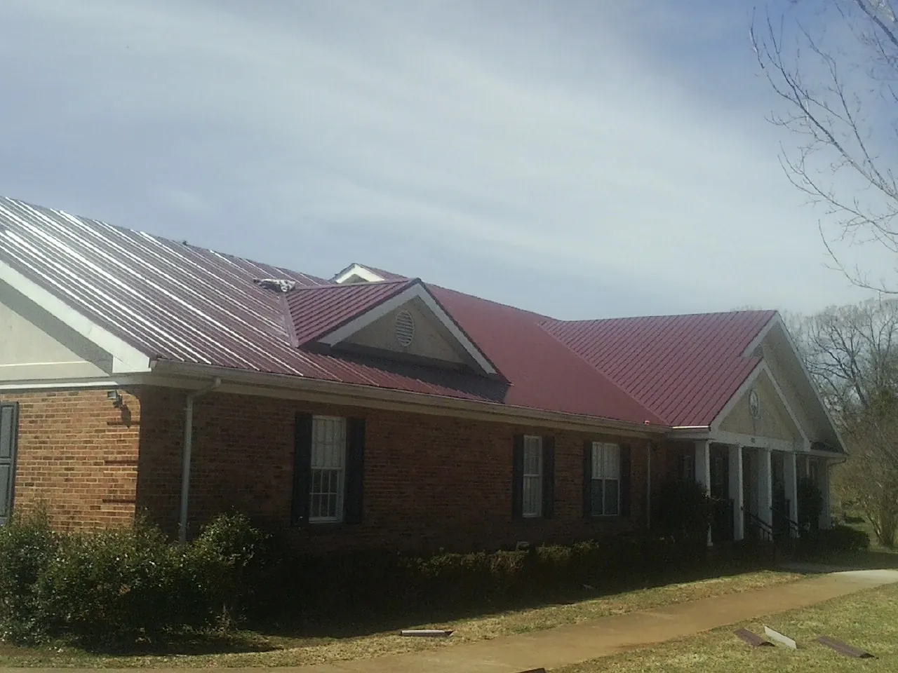 Red metal roof with gabled entries on a long brick building, from a Hail Damage Roof Repair job in Marmora