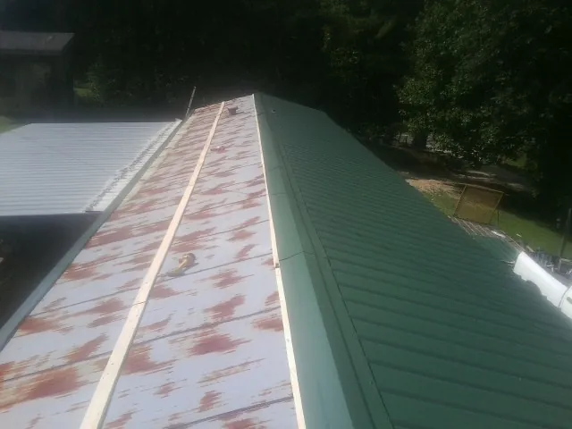 Old rusted panels beside newly installed green metal roofing — Wind Damage Roof Repair by Roofing Brothers in Marmora