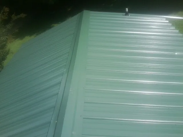 New green metal panels meeting at the ridge of a roof — Flat Roof Repair work by our crew in Marmora