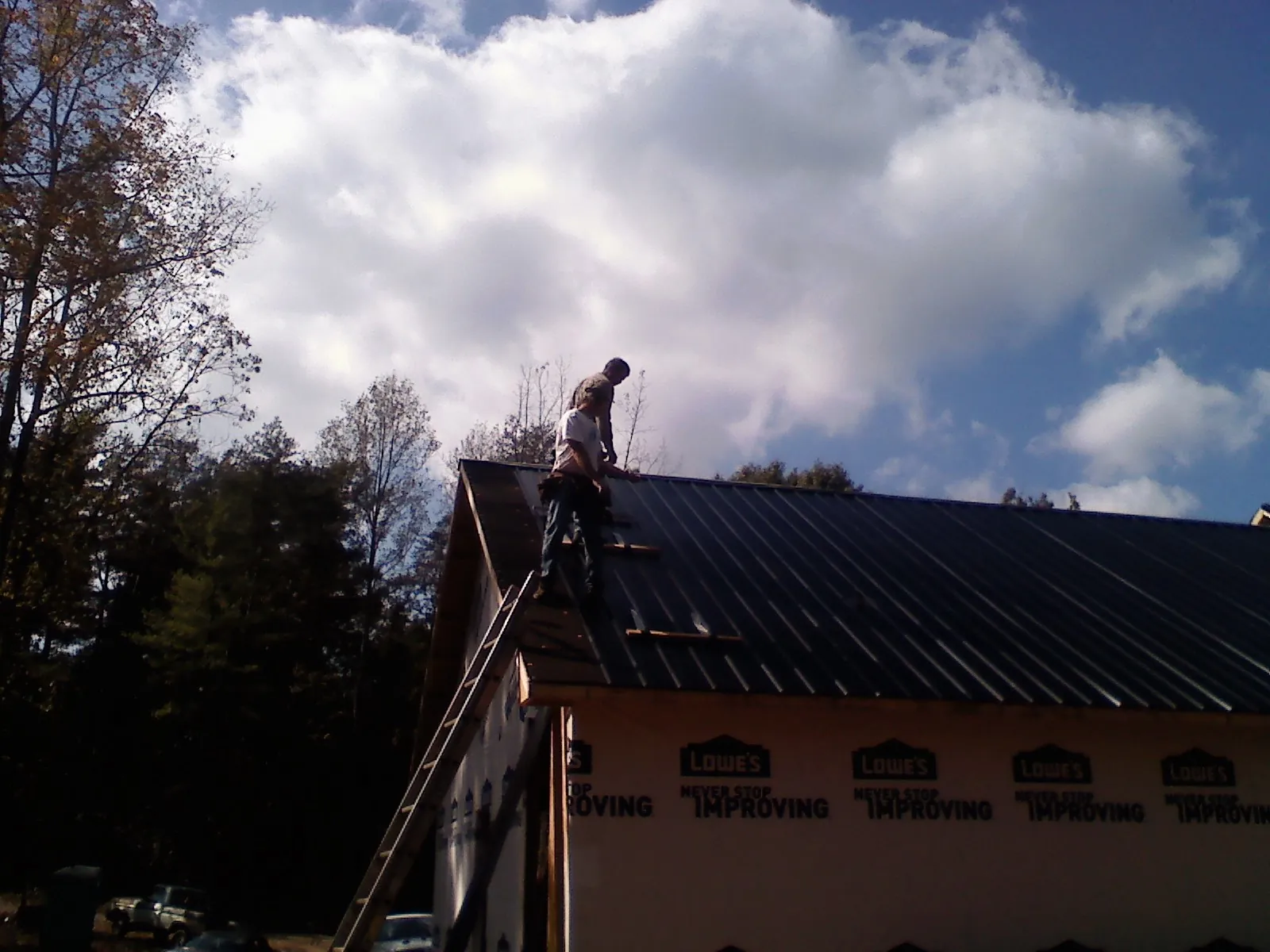 Roofer fastening dark metal panels high against a cloudy sky, from a Roof Inspection job in Marmora