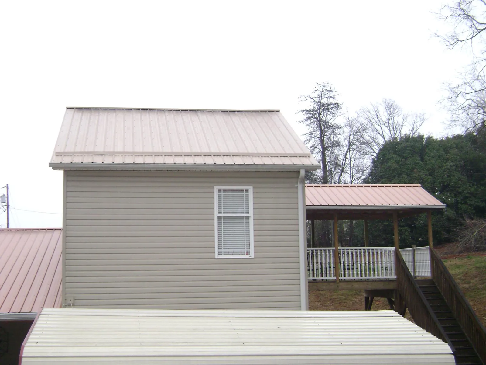 Tan metal roofs on a two story addition and attached porch, from a Roof Replacement job in Marmora